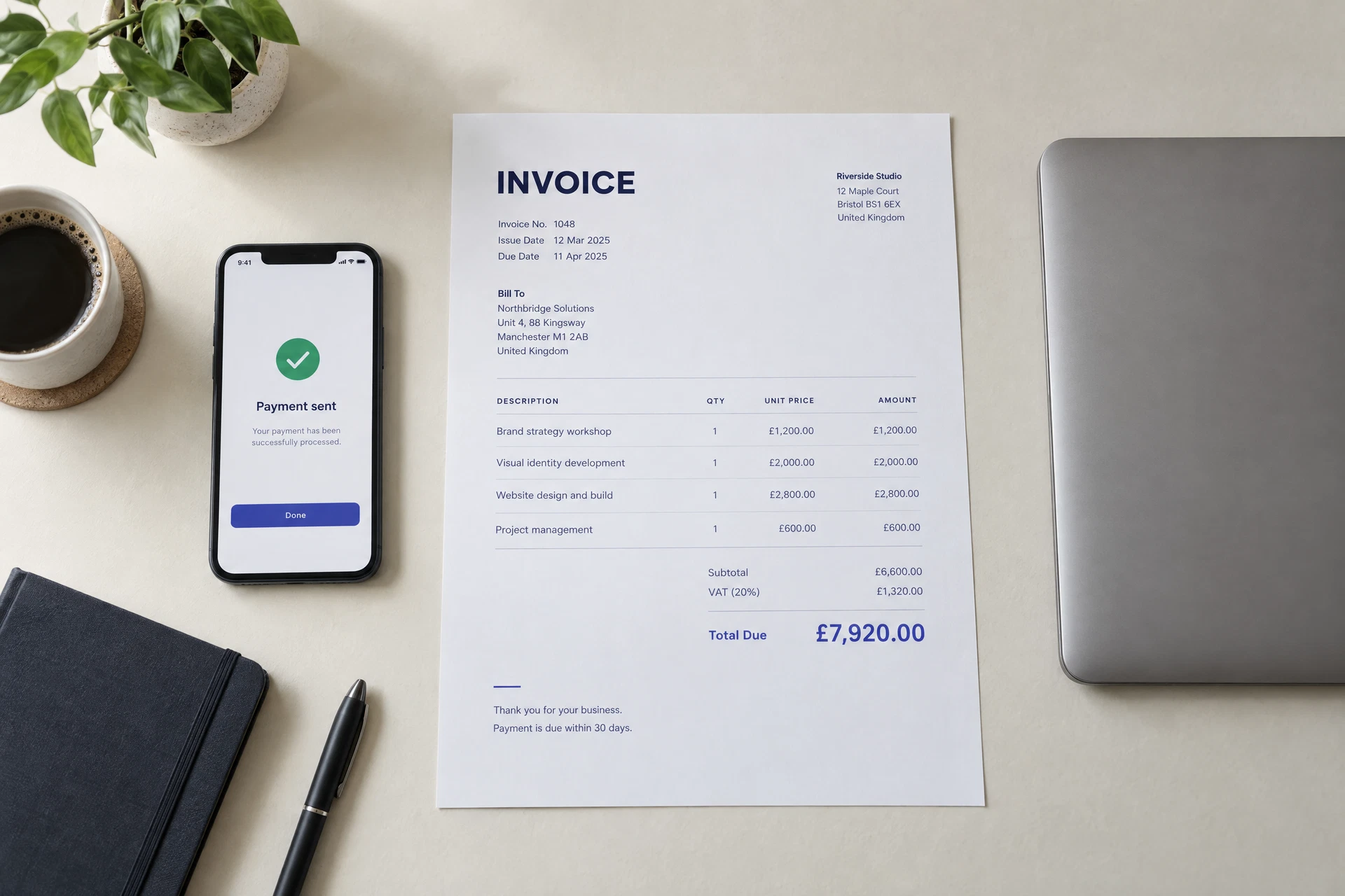 An invoice, a payment confirmation on a phone, and a laptop on a desk
